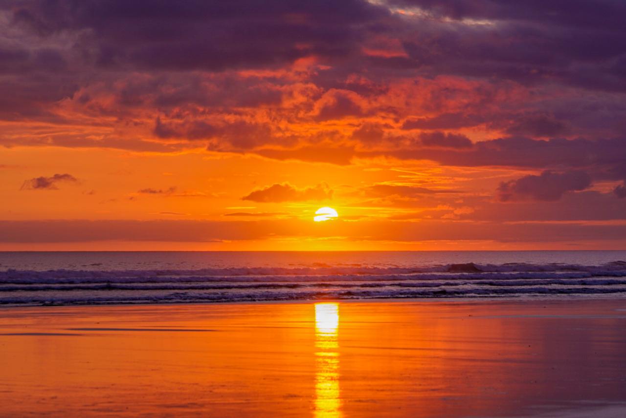 Orange sunset reflected on wet sand along the Pacific coast